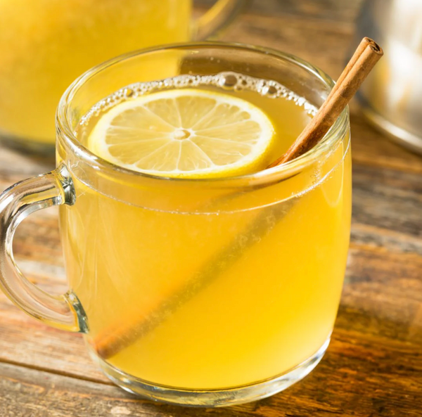 Glass mug with yellow liquid, lemon slice, and cinnamon stick on a wooden surface