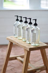 Set of clear bottles with black pumps on a wooden stool indoors.