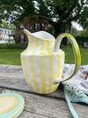 Yellow and white striped ceramic pitcher on a wooden surface with a blurred background