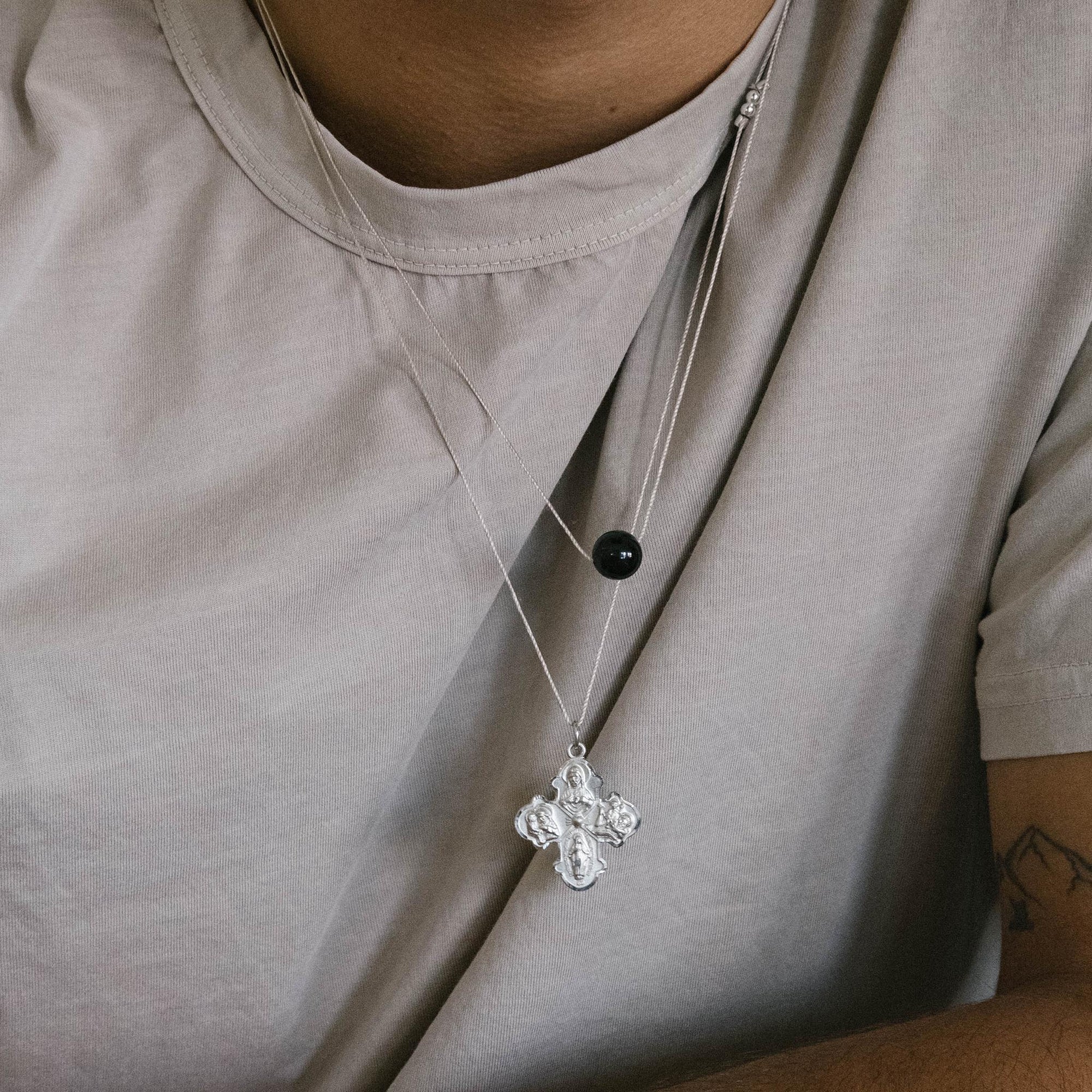 Silver necklace with a cross pendant on a person wearing a light gray shirt.