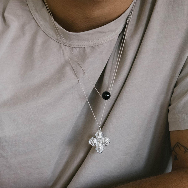 Silver necklace with a cross pendant on a person wearing a light gray shirt.