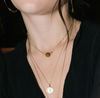 A person wearing a gold-colored adjustable necklace with a single slider bead, featuring a gemstone, and other gold necklaces layered over a shirt.