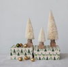 A cream-colored sisal bottle brush tree with a carved wooden base, displayed on a box decorated with Christmas trees.