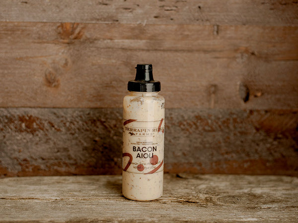 A bottle of bacon garnishing aioli squeeze with a wooden background.