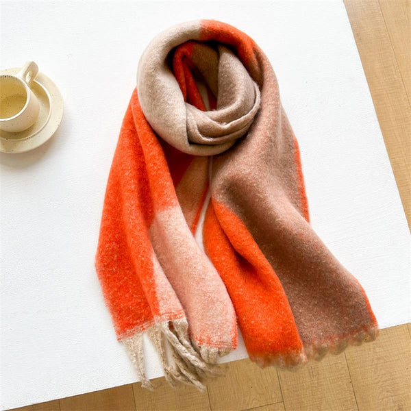 A soft, fuzzy scarf with a color-blocked pattern in orange, beige, and light pink, draped on a white table next to a small cup and saucer.