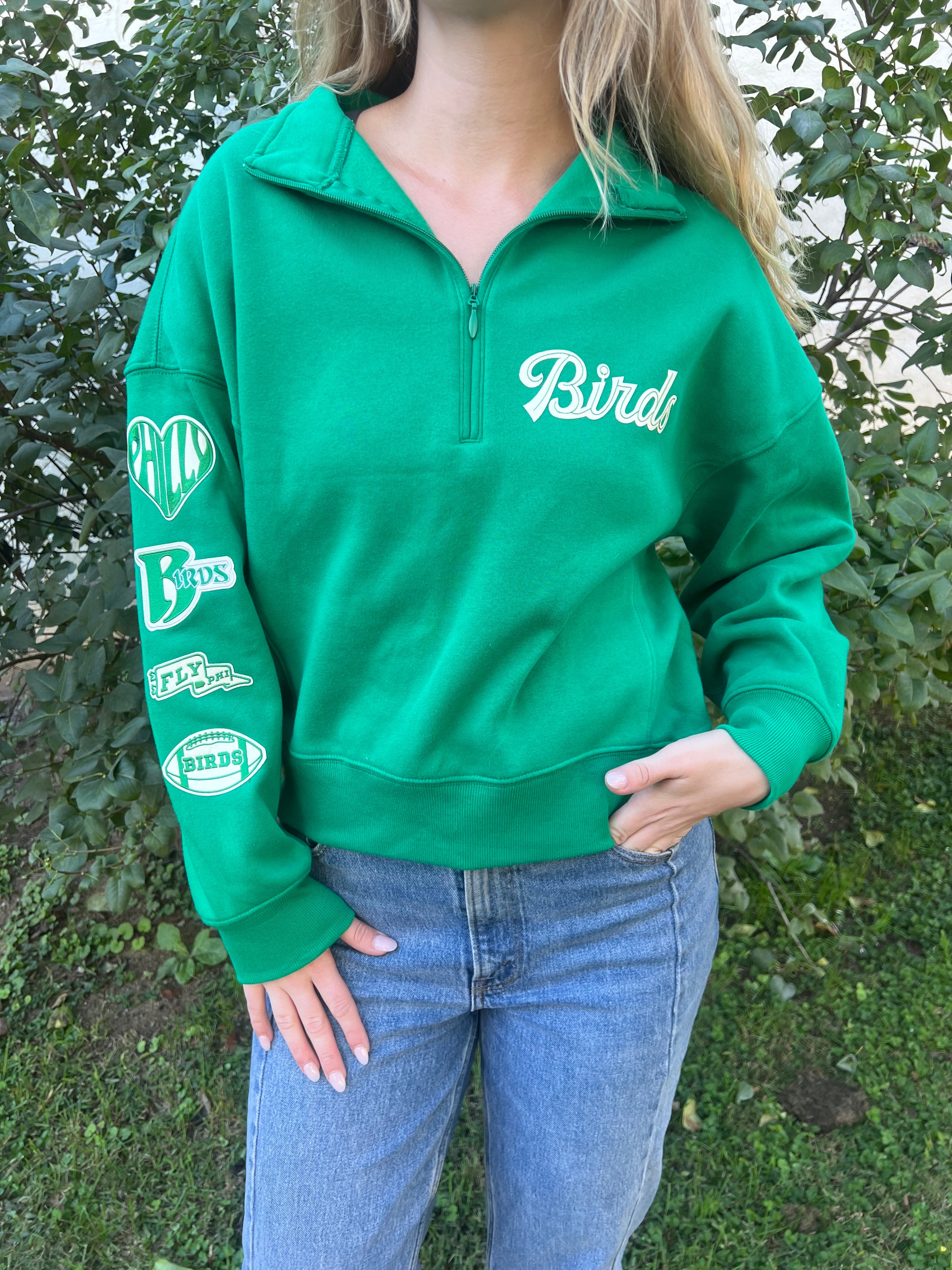 quarter zip sweatshirt featuring a sleeve of patches on a model standing outside
