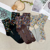 Set of floral-patterned socks on a textured surface with a plant and magazine in the background.