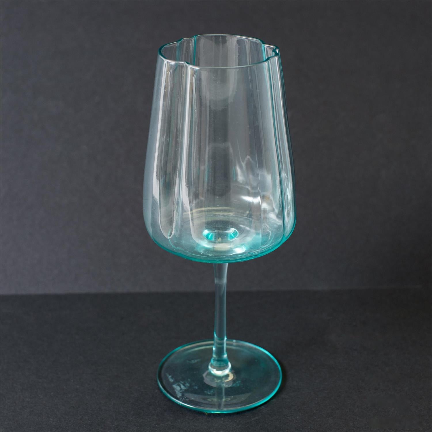 A clear glass goblet with a distinct turquoise-blue tint at the rim and base, set against a dark gray background.