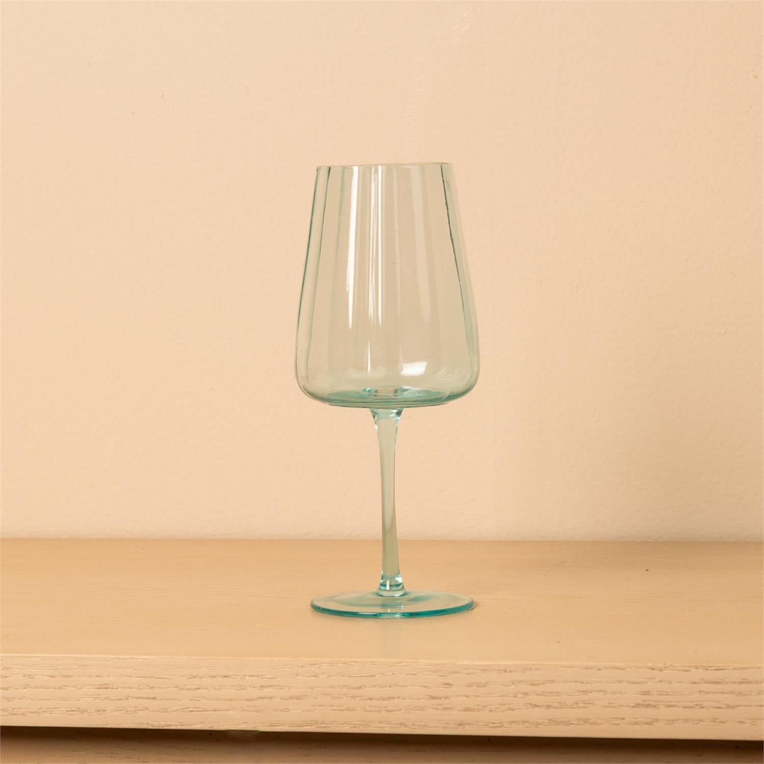 A clear wine glass with a light aqua tint, standing on a light wood surface against a solid beige background.
