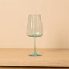 A clear wine glass with a light aqua tint, standing on a light wood surface against a solid beige background.