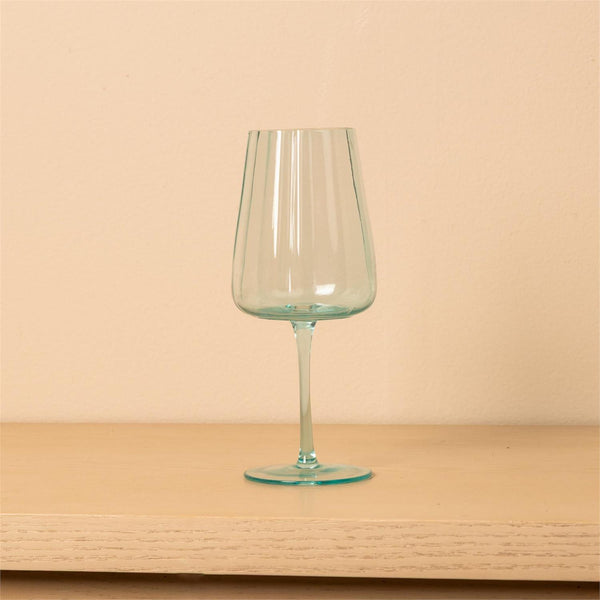 A clear wine glass with a light aqua tint, standing on a light wood surface against a solid beige background.