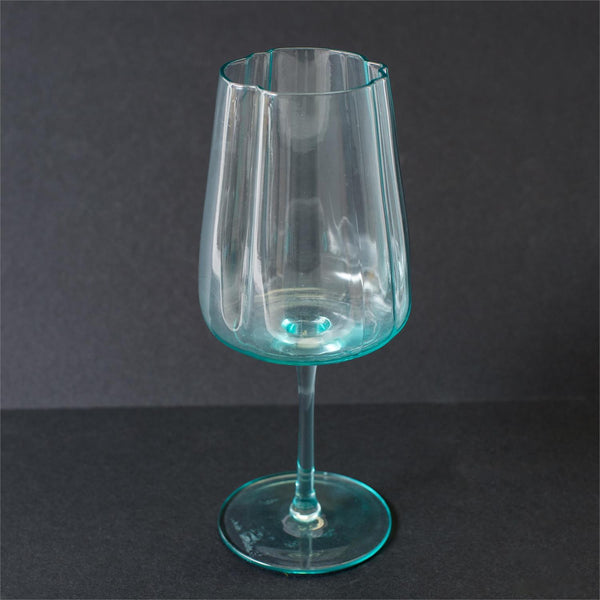 A clear glass goblet with a distinct turquoise-blue tint at the rim and base, set against a dark gray background.