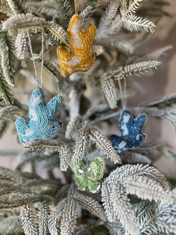 Assorted glass bead ornaments in the shapes of butterflies and doves, in blue, yellow, green, and pink colors, hanging from a Christmas tree.