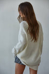 Woman wearing a white oversized sweater and polka dot shorts against a plain background