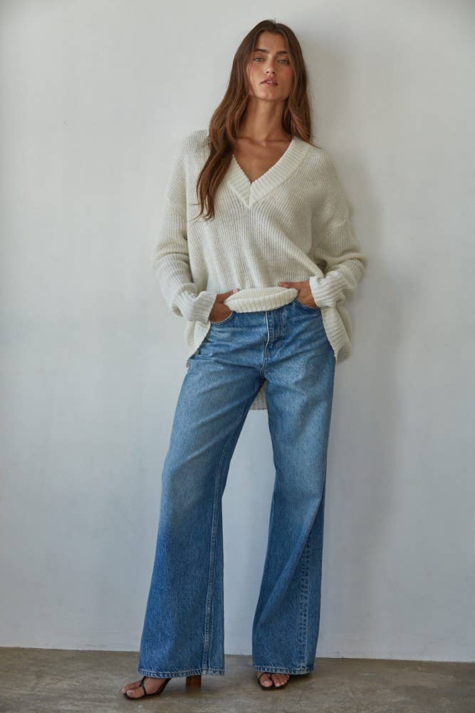 Woman wearing a cream sweater and blue jeans against a plain background