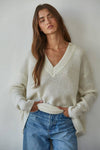 Woman wearing a cream sweater and blue jeans against a plain background