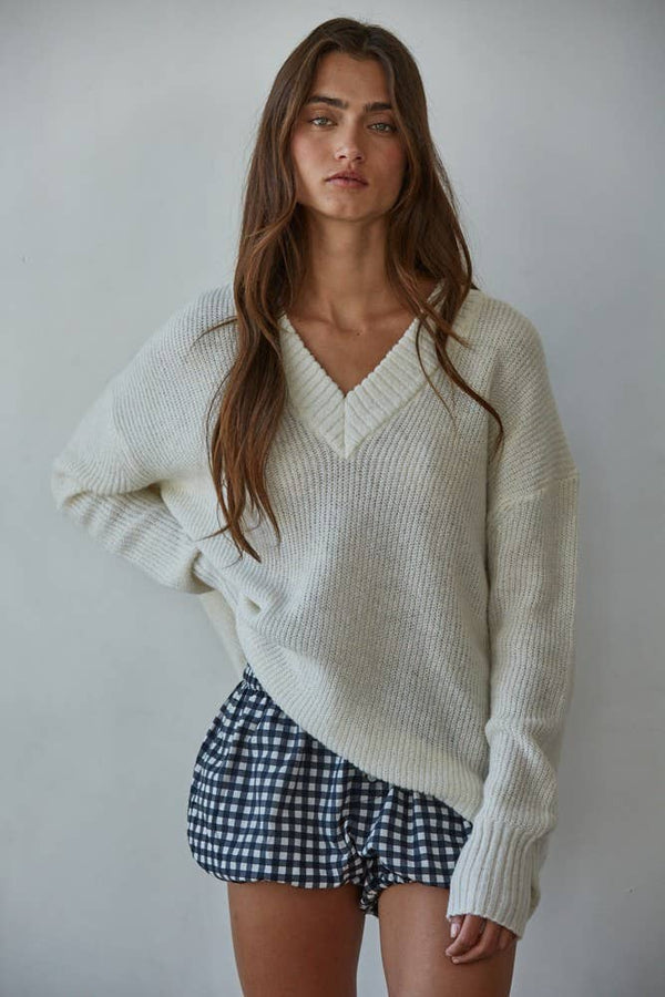 Woman wearing a white sweater and checkered shorts against a plain background