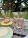 Two pink glass tumblers on a wooden surface with a blurred background