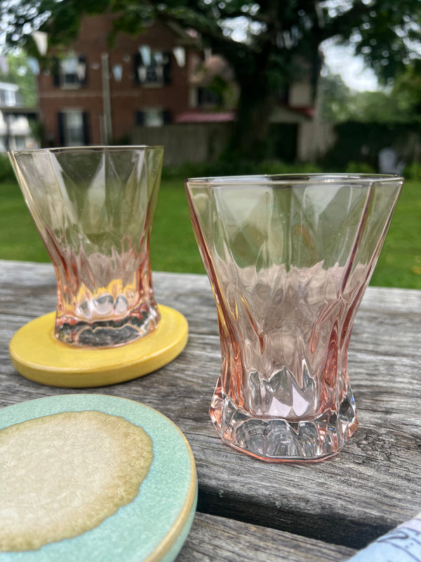 Two pink glass tumblers on a wooden surface with a blurred background