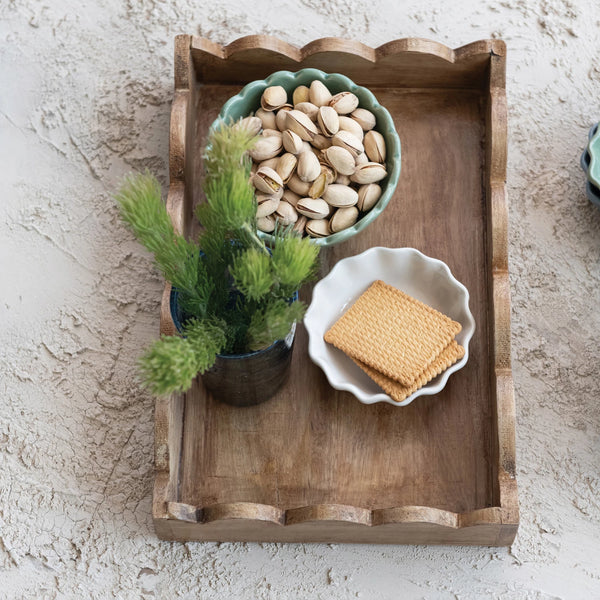 Wooden tray with a bowl of nuts, a potted plant, and a plate of cookies on a textured surface.