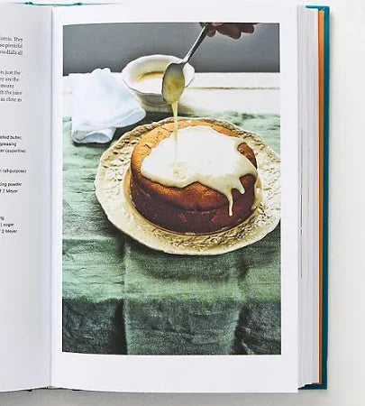 Open book showing a recipe for a dessert with a close-up of a cake being drizzled with syrup.
