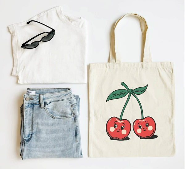 A tote bag with a vintage cherry design, displayed alongside a white T-shirt and a pair of blue denim jeans.
