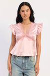 A woman modeling a light pink satin top with ruffled flutter sleeves, a lace V-neckline, and a lace horizontal band across the bust, paired with light-wash blue jeans against a plain white studio background.