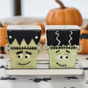 Halloween-themed Frankenstein salt and pepper shakers on a decorative stand with pumpkins in the background.