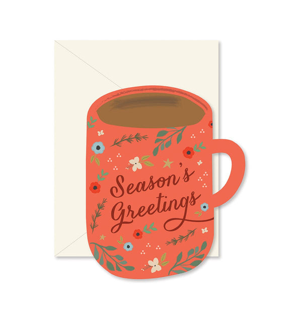 A die-cut greeting card featuring a coffee mug with 'Season's Greetings' written inside, decorated with floral patterns, and a beige envelope.