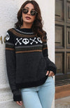 Person wearing a black sweater with skull and crossbones pattern, standing against a white wall.