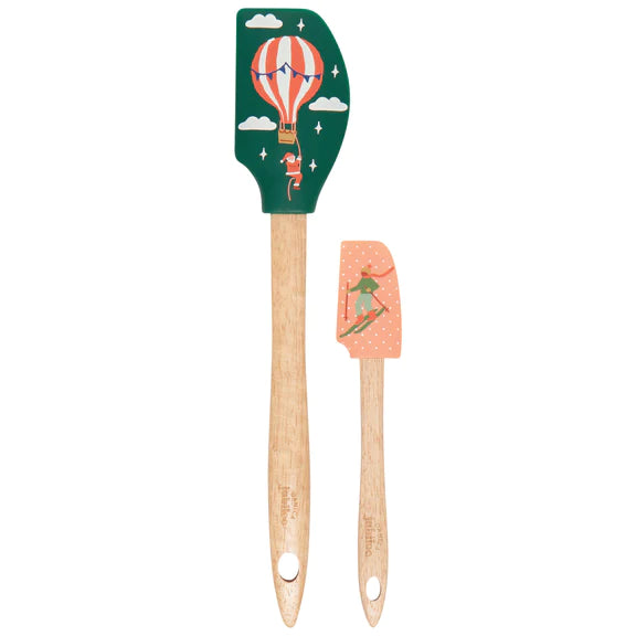 A set of two silicone spatulas with solid wood handles, one featuring a candy cane design and the other with a winter scene. Both have silicone heads and are decorated with illustrations of a snowman and a hot air balloon.