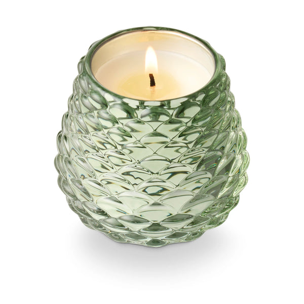 Green textured glass candle holder with a lit candle on a white background