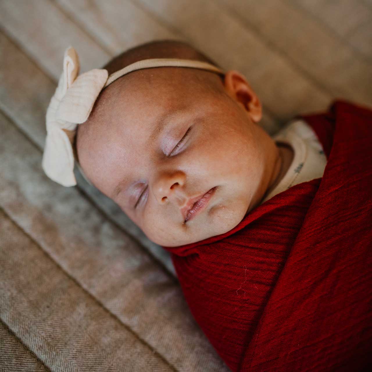 Newborn baby sleeping with a bow headband and red blanket