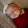 Newborn baby sleeping with a bow headband and red blanket