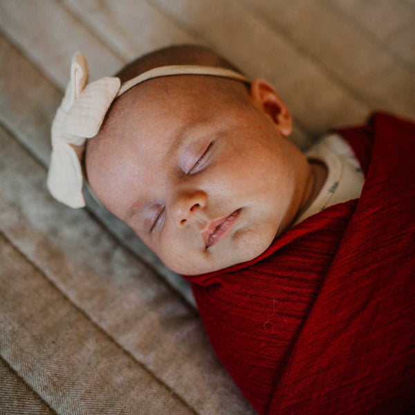 Newborn baby sleeping with a bow headband and red blanket
