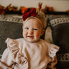 Child wearing a beige sweater and red headband with bow, sitting on a patterned couch.