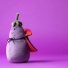 Plush toy shaped like an eggplant with a cape on a purple background