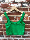 Green ribbed crop top on a wooden hanger against a brick wall.