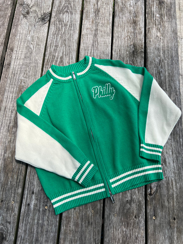 Green and white varsity jacket with 'Philly' text on a wooden surface