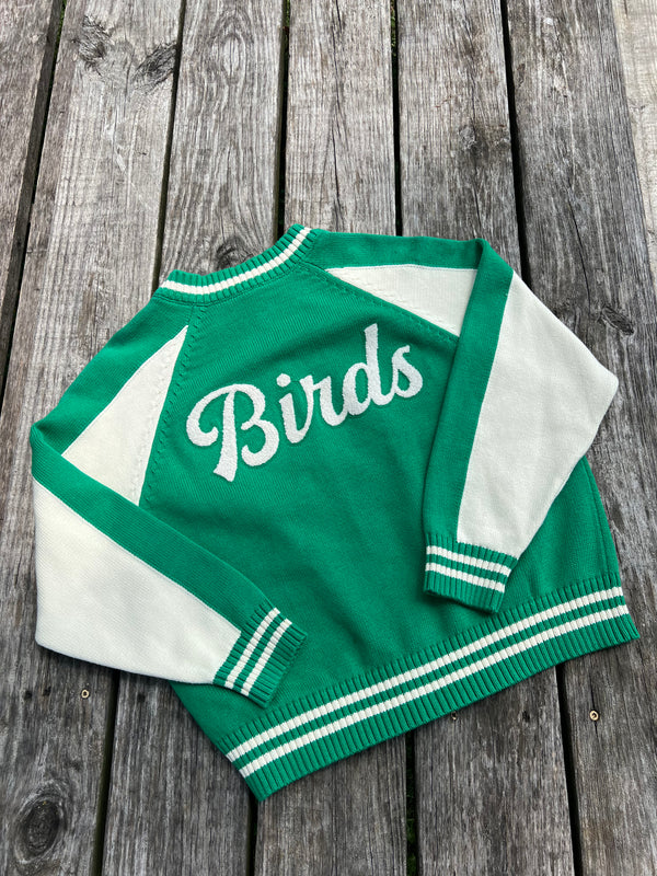Green and white varsity jacket with 'Birds' text on a wooden surface