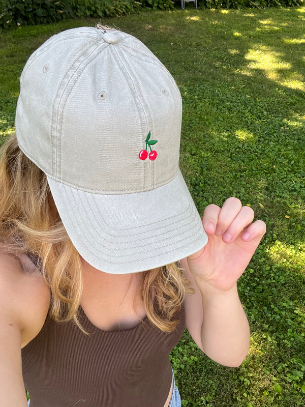 Person wearing a light gray cap with cherry design outdoors on grass