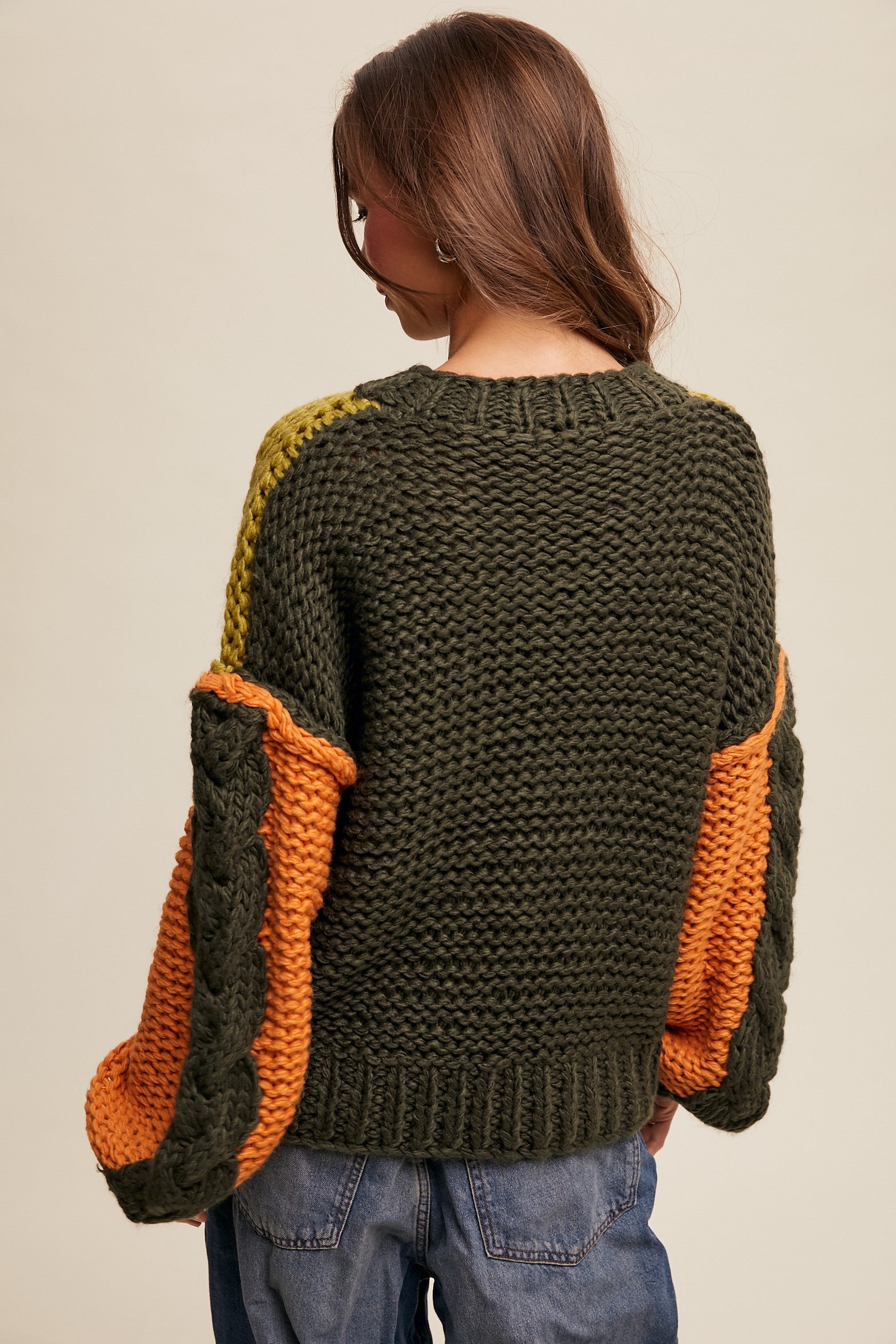 Person wearing a green and orange knitted sweater on a beige background