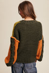Person wearing a green and orange knitted sweater on a beige background