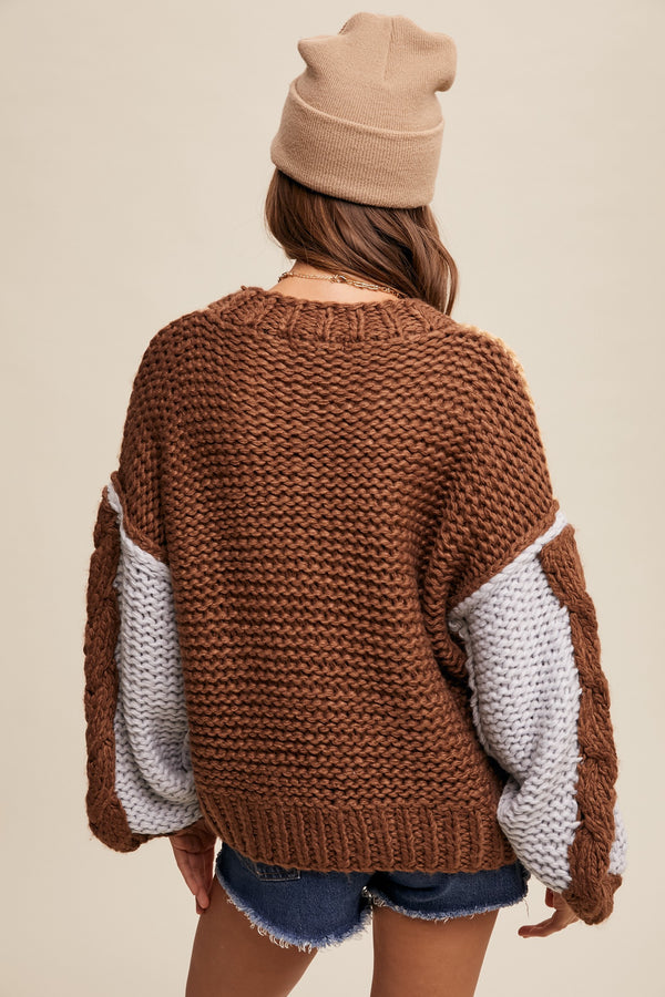 Person wearing a brown knitted sweater with white sleeves and a beige beanie on a beige background