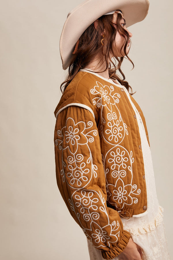 Woman wearing a brown embroidered jacket with a beige hat on a beige background