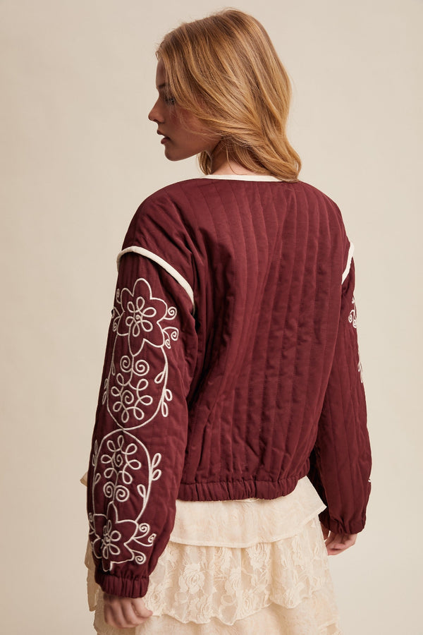Woman wearing a burgundy sweater with white embroidery on a beige background
