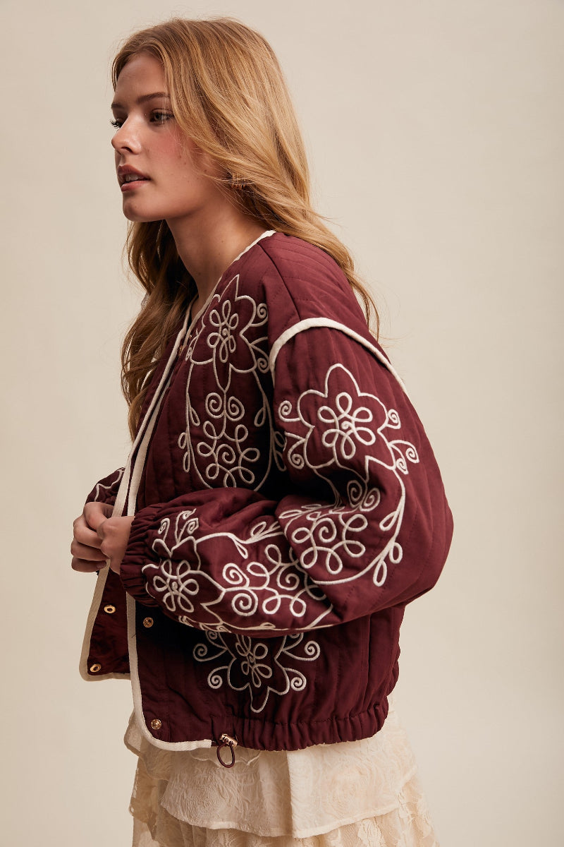Woman wearing a burgundy embroidered jacket against a beige background