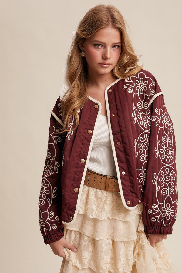 Woman wearing a maroon embroidered jacket with a beige background