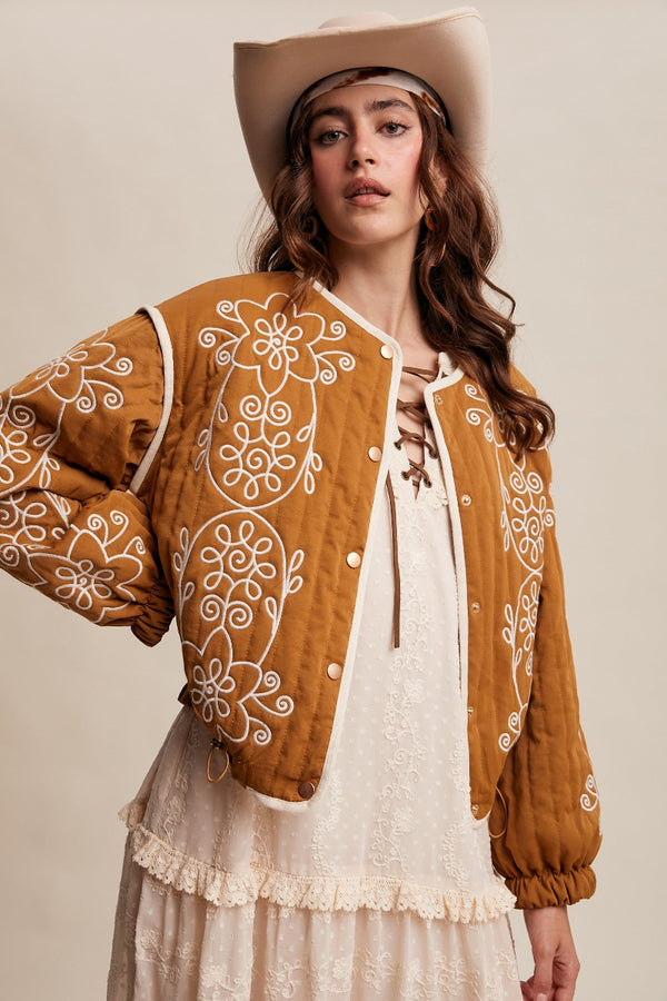 Woman wearing a brown embroidered jacket and white dress with a beige background