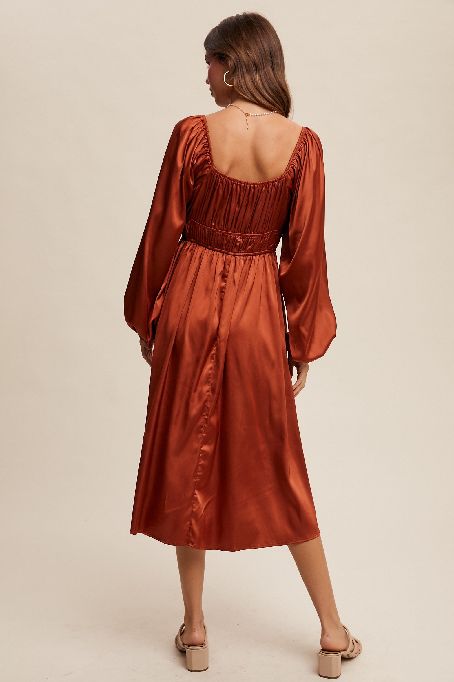 Woman wearing a rust-colored satin dress with long sleeves on a beige background